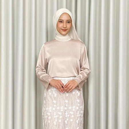 Woman wearing a beige top by Kartinis Label and white hijab with a white skirt against a light curtain background