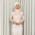 Woman wearing a beige top by Kartinis Label and white hijab with a white skirt against a light curtain background