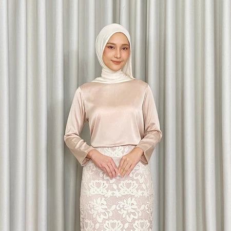 Woman wearing a cream-colored top by Kartinis Label and white lace skirt against a gray curtain background