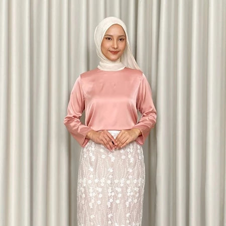 Woman wearing a dusty pink top by Kartinis Label and white hijab with a white skirt against a beige curtain background