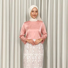 Woman wearing a dusty pink top by Kartinis Label and white hijab with a white skirt against a beige curtain background