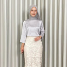 Woman wearing a light gray hijab, light gray top by Kartinis Label, and white lace skirt against a striped curtain background.