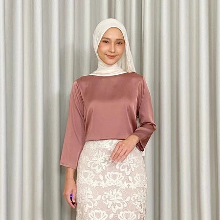 Woman wearing a terracota-colored top by Kartinis Label and white lace skirt against a plain background