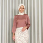 Woman wearing a terracota-colored top by Kartinis Label and white lace skirt against a plain background