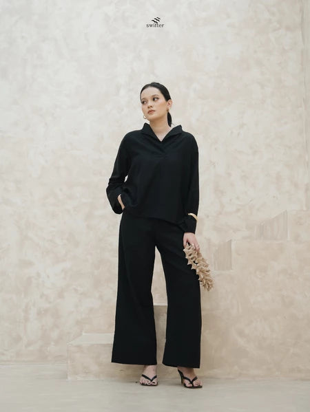 Woman wearing a black blouse by Swifter and black pants against a light beige wall