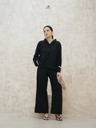 Woman wearing a black blouse by Swifter and black pants against a light beige wall