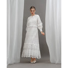 Woman wearing a white lace dress by Kasa Heritage standing between two white curtains.