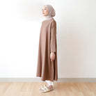 Seorang wanita memakai tunik berlengan panjang berwarna coklat, hijab, dan celana panjang.