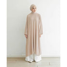 Seorang wanita memakai tunik berlengan panjang berwarna beige muda, hijab, dan celana panjang.