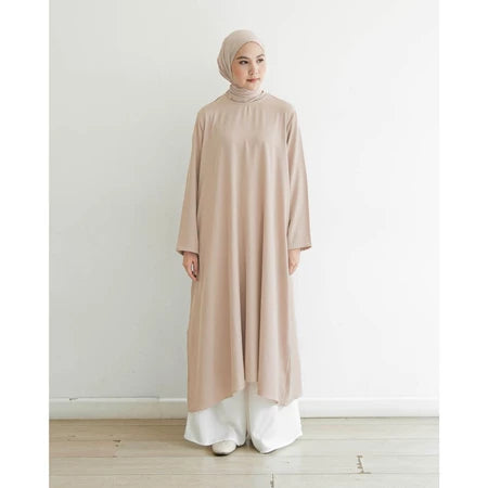 Seorang wanita memakai tunik berlengan panjang berwarna beige muda, hijab, dan celana panjang.