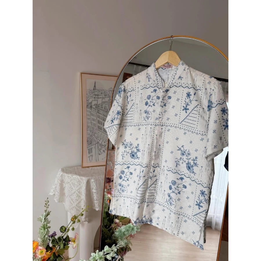 Cream blue floral patterned shirt by Haidee Orlin on a hanger in front of a mirror with decorative elements.