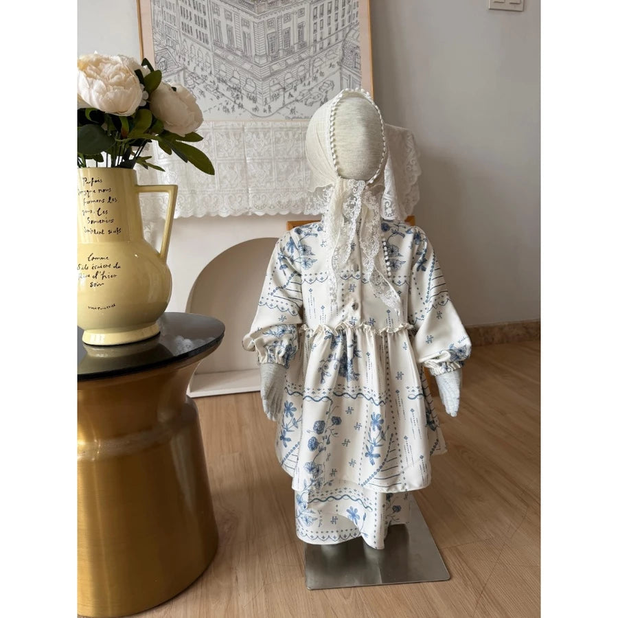 Mannequin wearing a cream blue floral dress by Haidee Orlin in a room with a vase and decorative items.