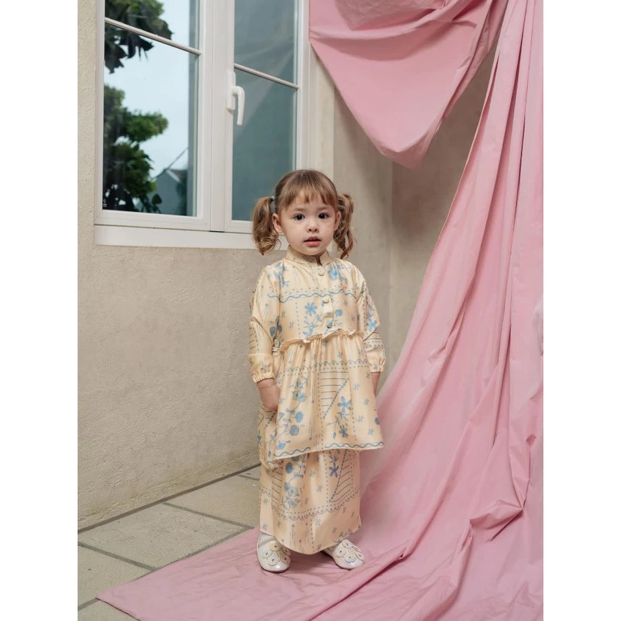 Young girl in a yellow floral dress by Haidee Orlin standing on a pink mat next to a window with pink curtains.