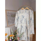 Cream blue floral tunic by Haidee Orlin on a hanger with a decorative background
