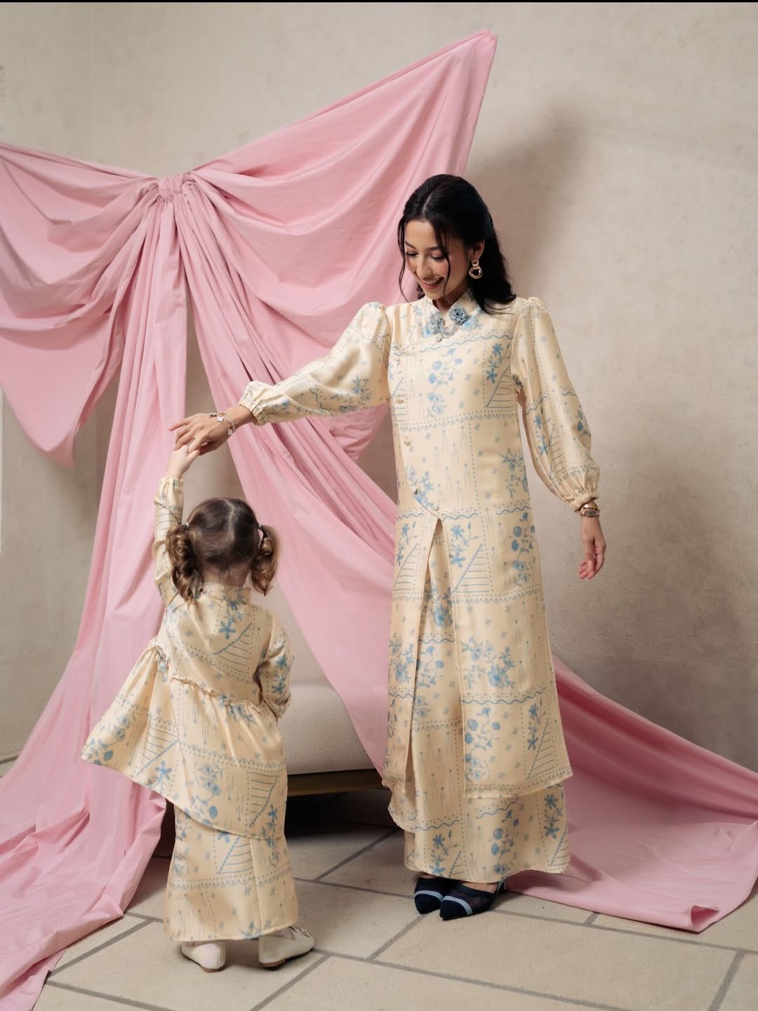 Woman and child in matching yellow floral tunic by Haidee Orlin standing in front of a pink curtain.