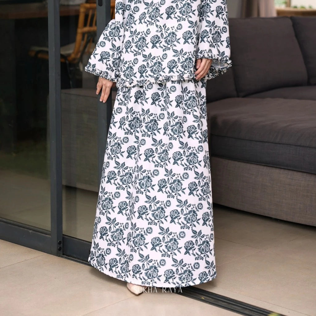 A person wearing a long floral skirt with a blue color scheme, featuring an A-line silhouette from BWBYAZ.