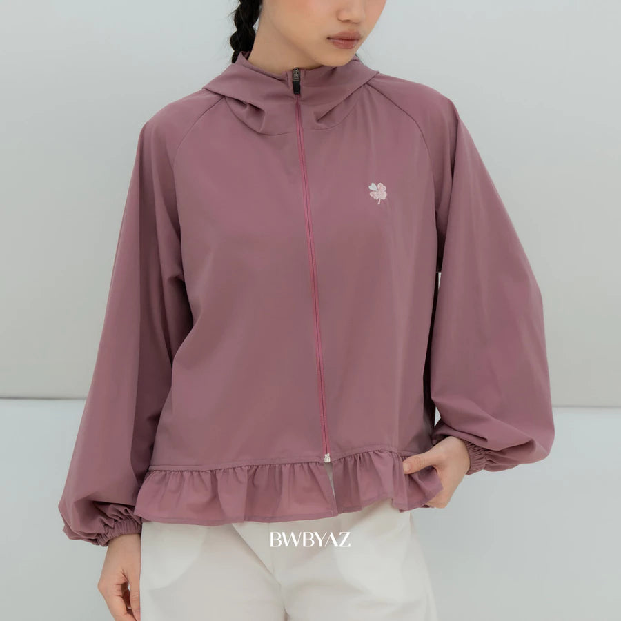 A model wearing a soft mauve lightweight hooded jacket by BWBYAZ with a small embroidered flower on the left chest, paired with white pants. The brand name 'BWBYAZ' is printed at the bottom.