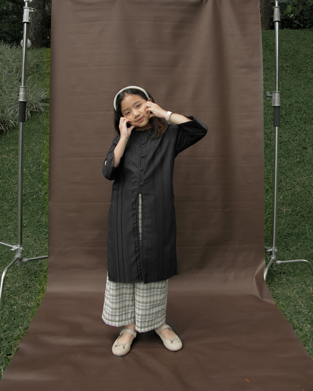 Person wearing a dark coat and plaid pants by Mistyvori standing in front of a brown backdrop with photography equipment around.