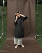 Person wearing a dark coat and plaid pants by Mistyvori standing in front of a brown backdrop with photography equipment around.