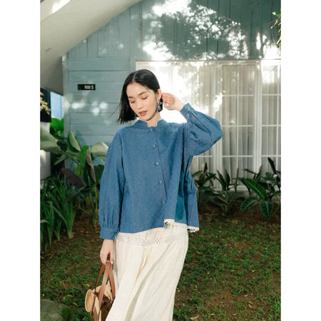 Woman wearing a blue top from Haidee Orlin and white pants outdoors with greenery around