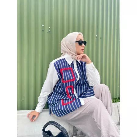 Person wearing a blue and white striped shirt by Abame and sunglasses, standing against a green fence.