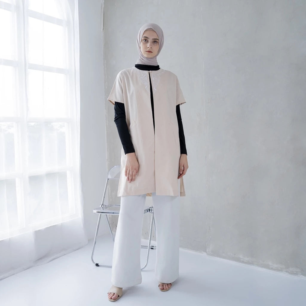 A woman wearing a beige linen tunic with short sleeves.

Seorang wanita memakai tunik linen berwarna beige berlengan pendek.