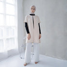 A woman wearing a beige linen tunic with short sleeves.

Seorang wanita memakai tunik linen berwarna beige berlengan pendek.