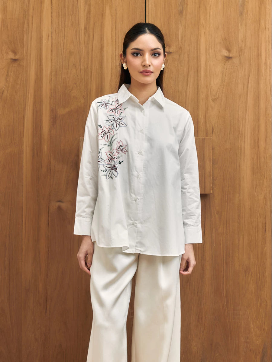 Woman wearing a white shirt with floral embroidery by Studio Tui against a wooden background