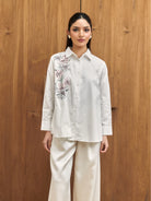 Woman wearing a white shirt with floral embroidery by Studio Tui against a wooden background
