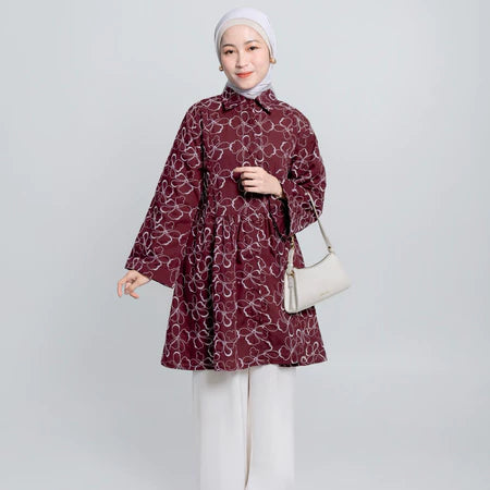 Woman wearing a patterned red tunic and white hijab on a light gray background