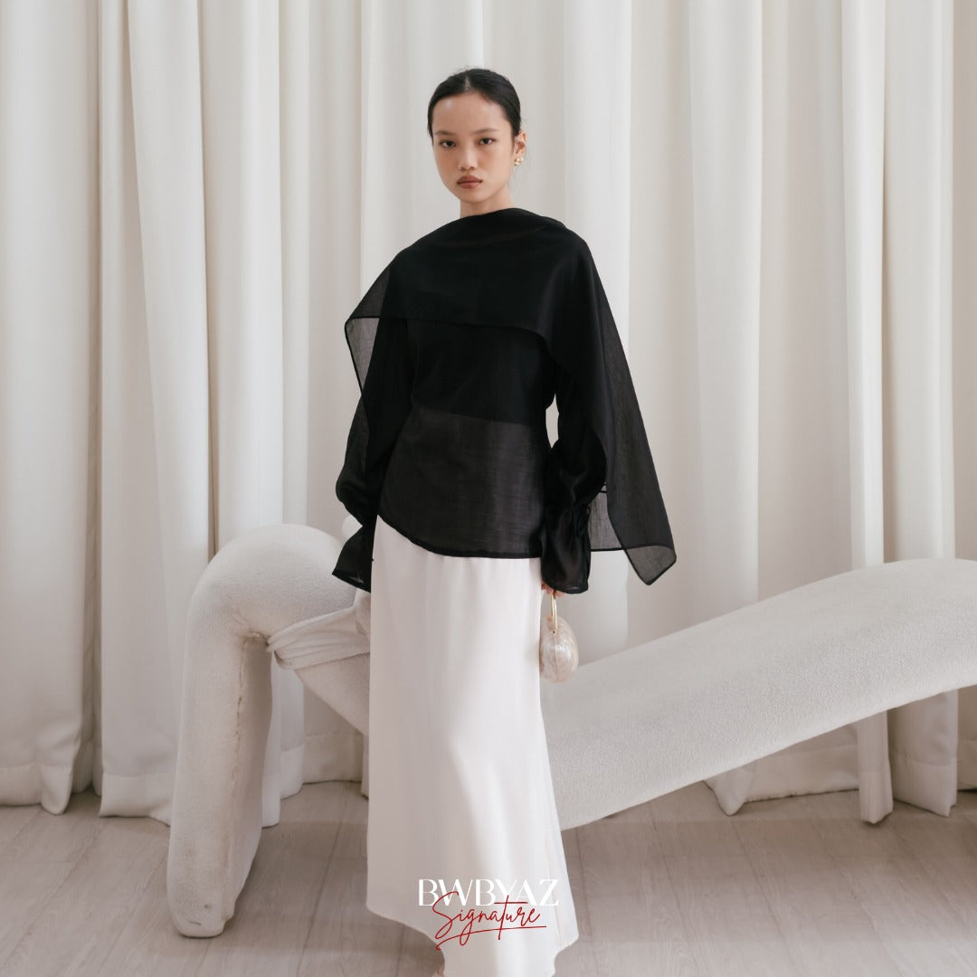 A model wearing a black shawl top with long sleeves and a separate shawl from BWBYAZ, standing in a room with a chair and a plain background.