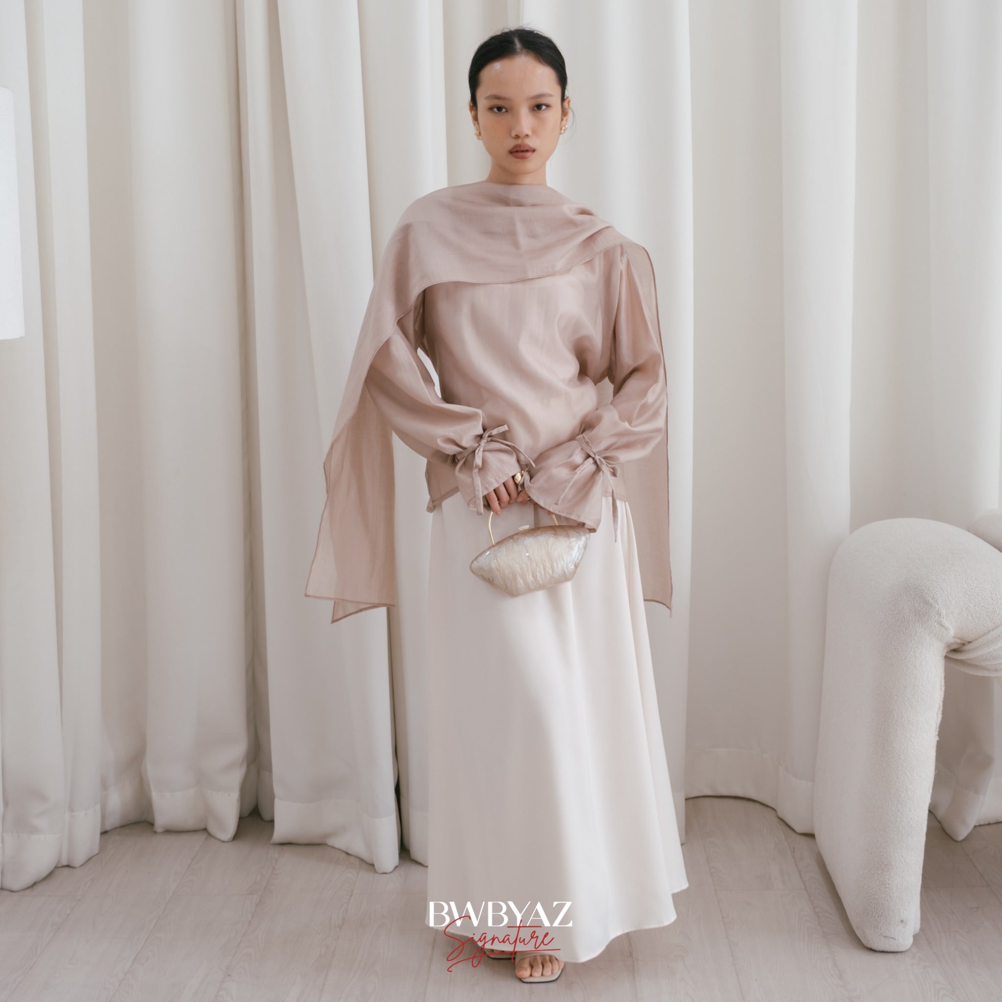A model wearing a ivory shawl top with long sleeves and a separate shawl from BWBYAZ, standing in a room with a chair and a plain background.