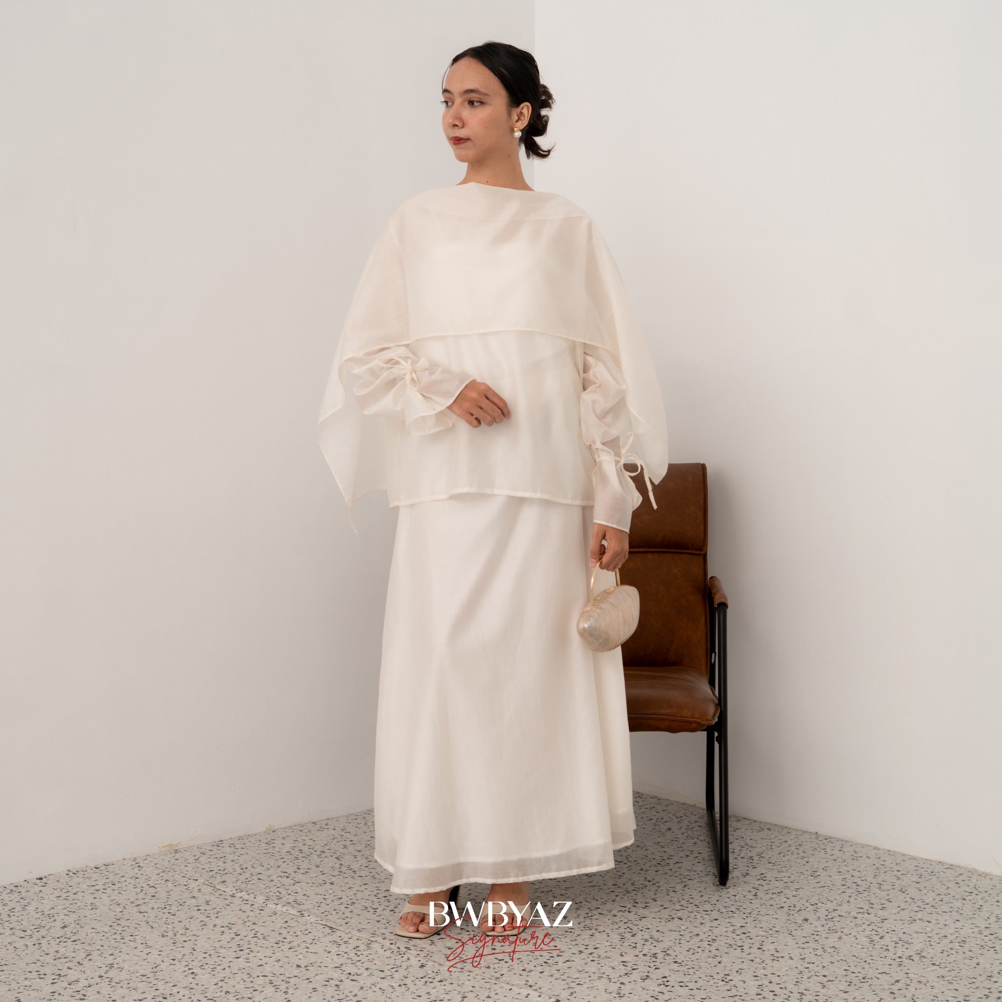 A model wearing a white shawl top with long sleeves and a separate shawl from BWBYAZ, standing in a room with a chair and a plain background.
