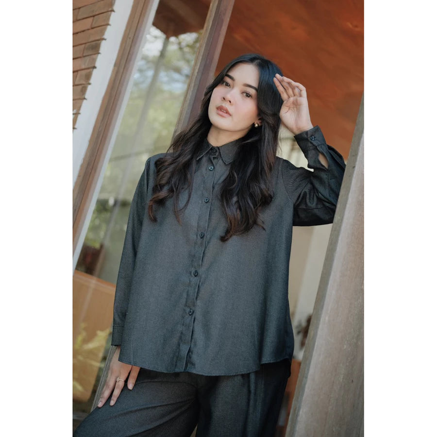 Woman wearing a dark grey shirt by Renaette and black pants standing indoors with a blurred background