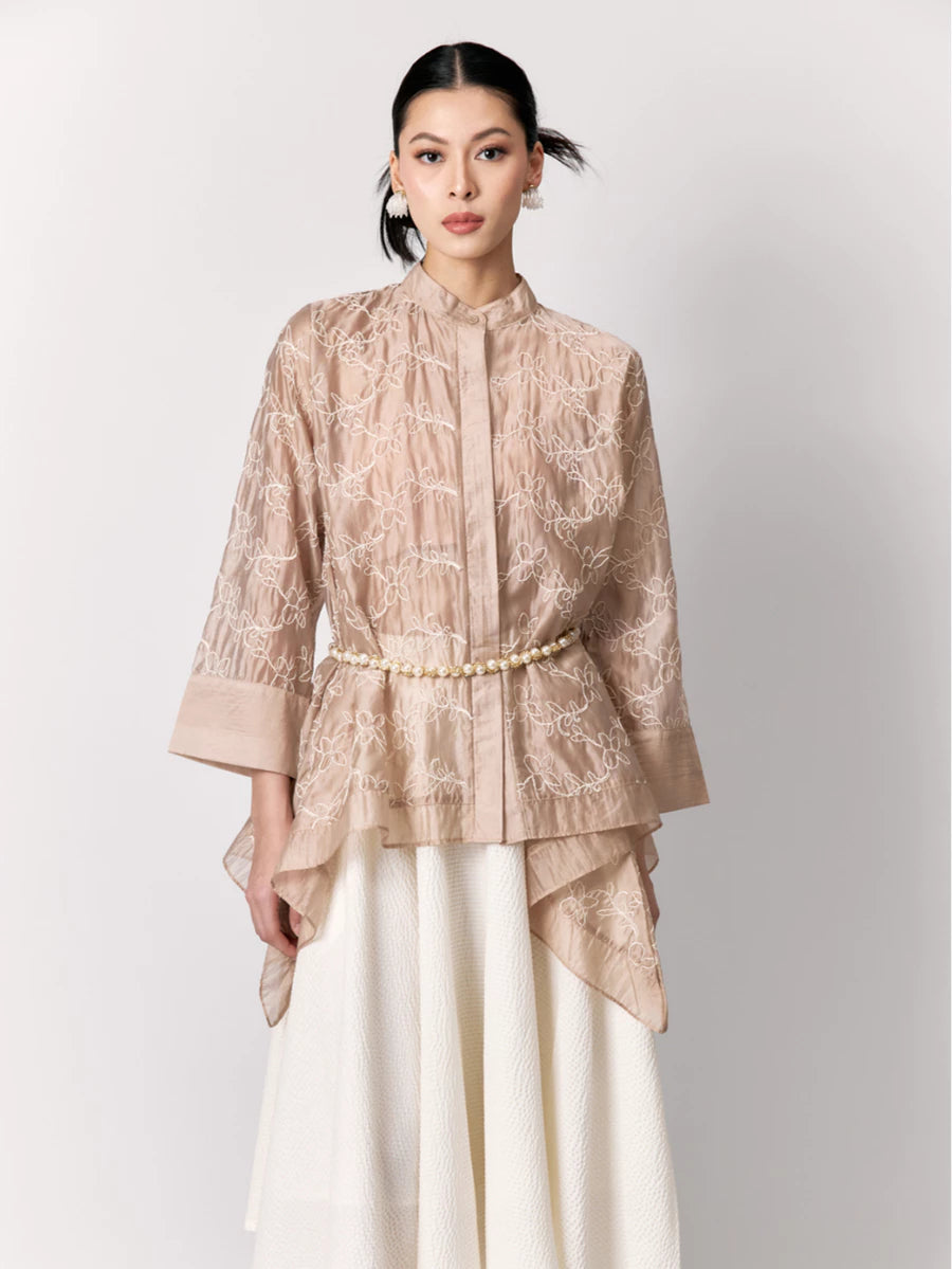 Woman wearing a beige lace shirt by Studio Tui with a pearl belt on a white background