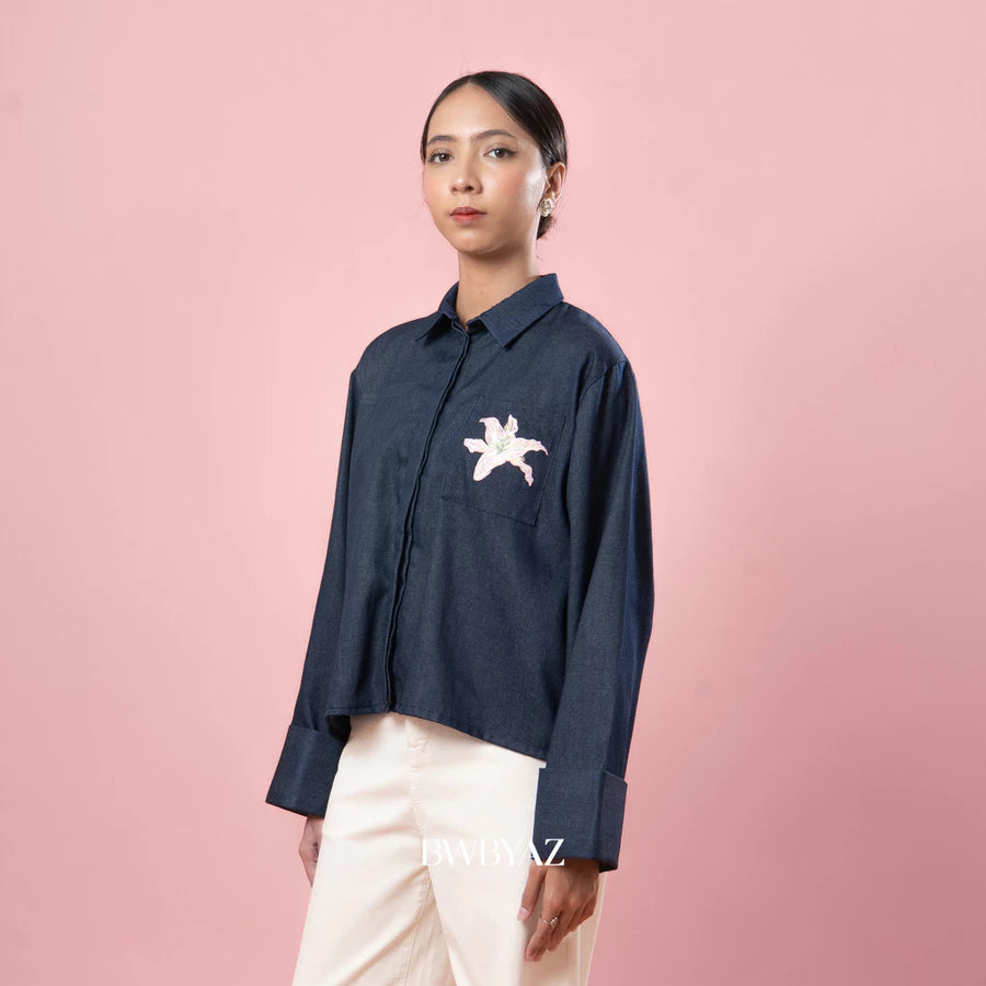 Person wearing a navy blue shirt with a small white floral embroidery by BWBYAZ on a pink background