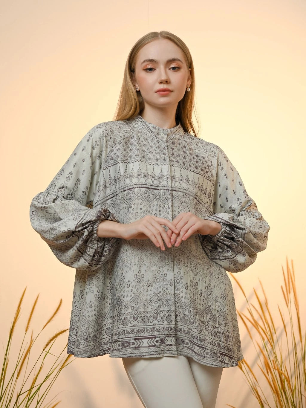 A woman wearing a light aqua colored Kamari blouse by Kasa Heritage with ethnic print and puffy sleeves, standing against a neutral backdrop.