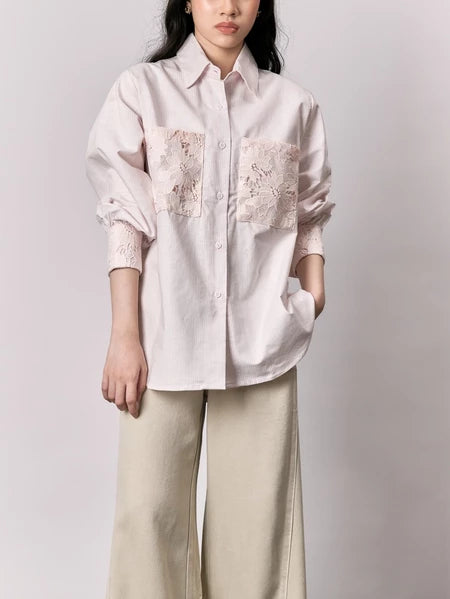 Person wearing a light pink shirt with floral embroidery and beige pants by Studio Tui on a plain background