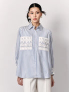 Woman wearing a blue and white striped shirt by Studio Tui with lace details on a plain background