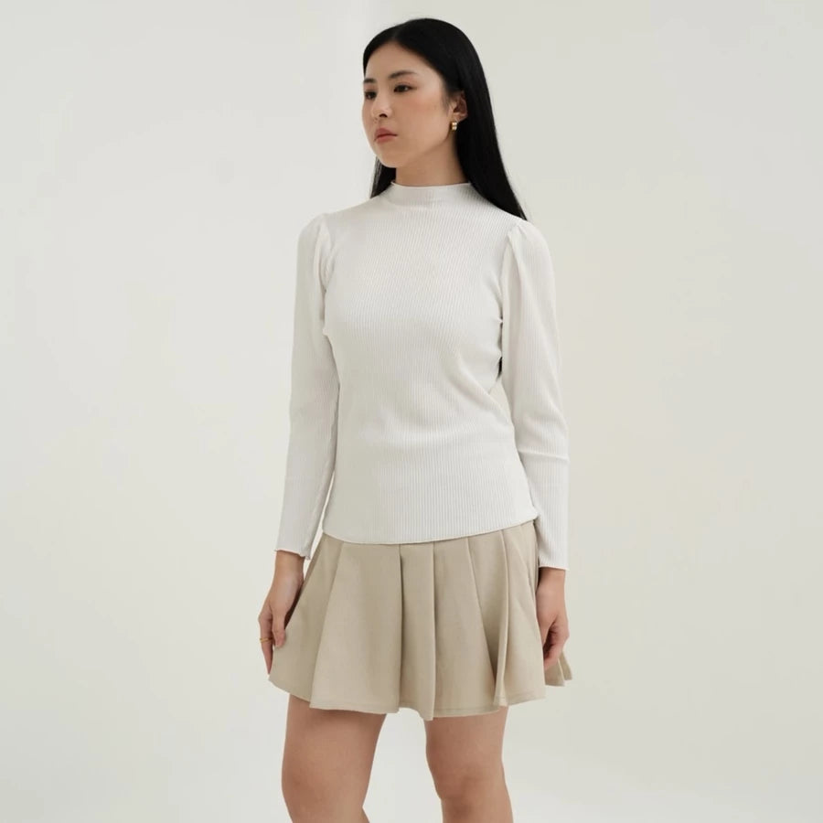 Woman wearing a white long-sleeved top by Tunique and beige skirt on a plain background