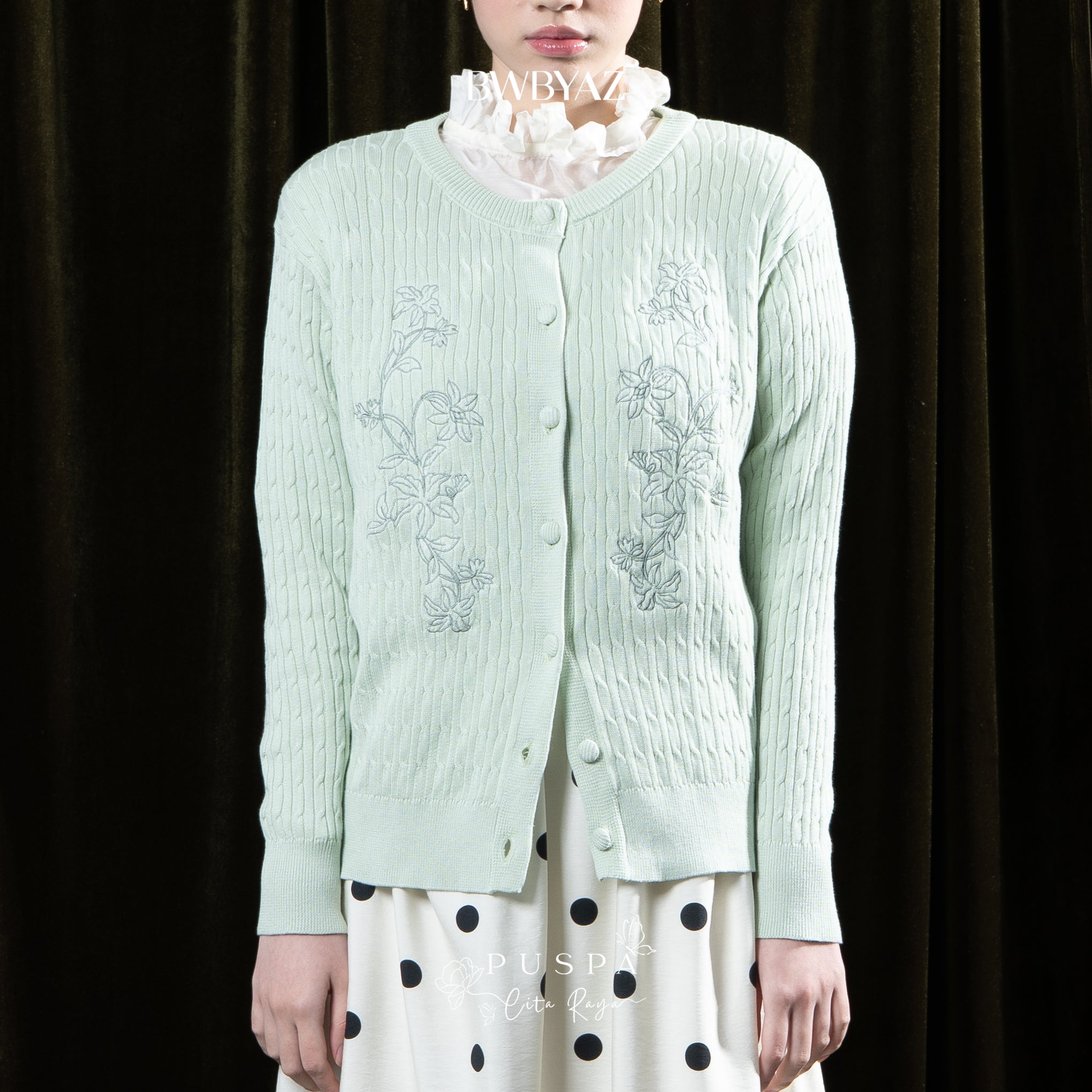 Person wearing a light green embroidered cardigan by BWBYAZ over a white blouse with black polka dots on a dark background.