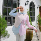 Woman wearing a light blue and pink blouse by Tunique with a hijab, standing outdoors.