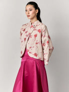 Woman wearing a floral blazer by Studio Tui and pink skirt on a gray background