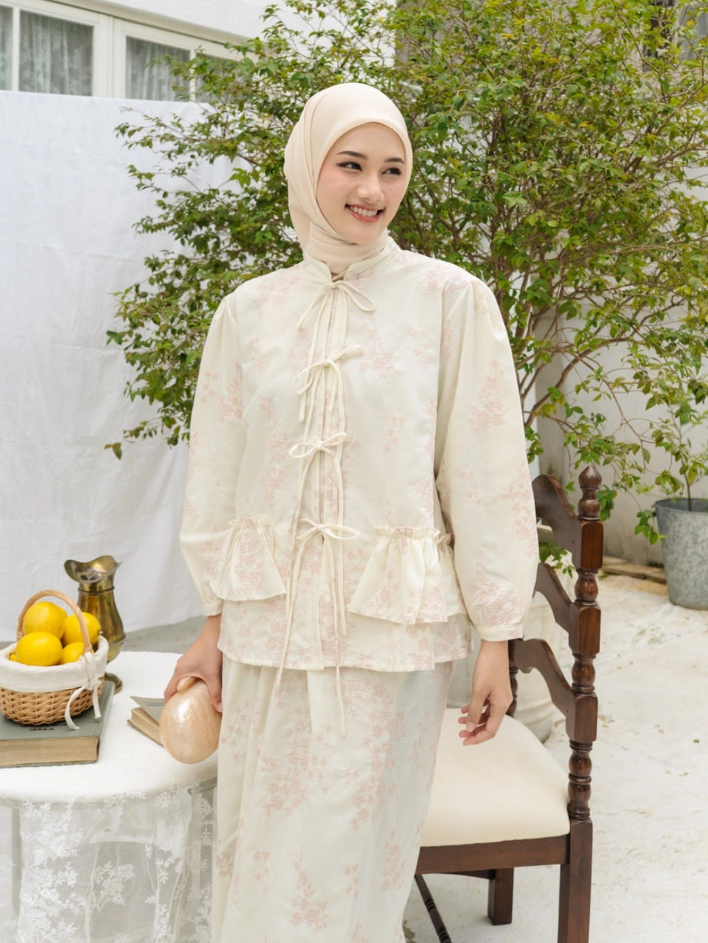 Woman wearing a ivory-colored traditional outfit by Haidee Orlin with a hijab, standing in an outdoor setting.