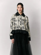 Woman wearing a floral shirt by Studio Tui with black collar and cuffs and a black skirt on a light gray background