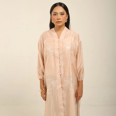 Woman wearing a peach colored embroidered kebaya by Kartinis Label against a beige background