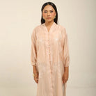 Woman wearing a peach colored embroidered kebaya by Kartinis Label against a beige background