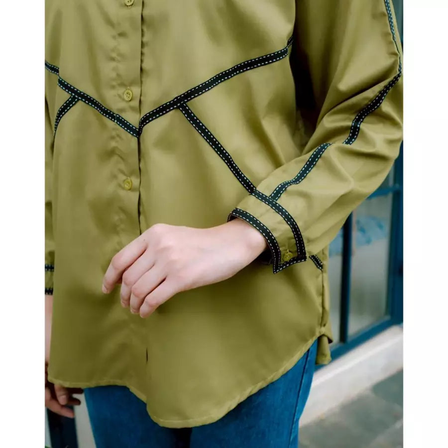 Green shirt by Abame with black trim worn by a person, blurred background