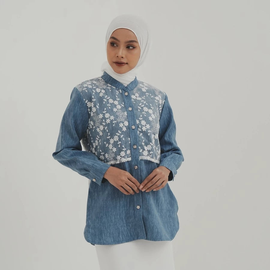 Woman wearing a blue denim shirt with floral embroidery by Tunique on a plain background
