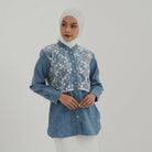 Woman wearing a blue denim shirt with floral embroidery by Tunique on a plain background
